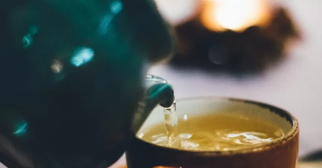 Warm close-up image of green tea being poured into a teacup with blurred background ambiance.